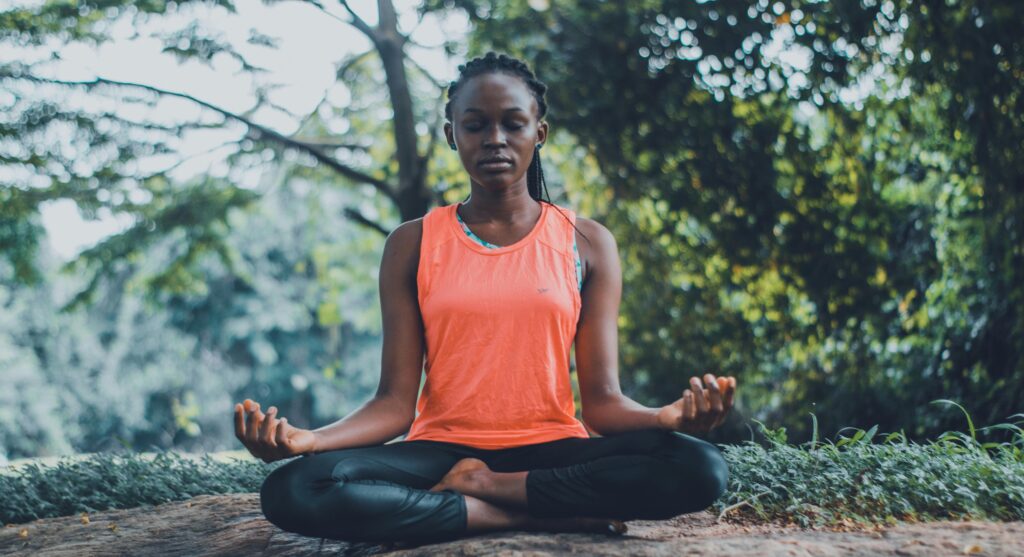 A woman meditating peacefully outdoors in a lush green setting, promoting relaxation and mindfulness.